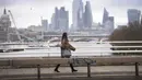Seorang wanita yang mengenakan masker berjalan di atas Waterloo Bridge yang kosong, London, Inggris, 12 Januari 2021. Inggris sedang menerapkan lockdown nasional ketiga untuk mengekang penyebaran virus corona COVID-19. (Victoria Jones/PA via AP)