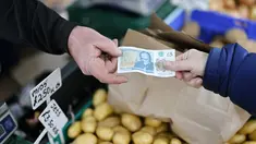 Seorang pelanggan memberikan uang kertas lima pound kepada pemilik kios untuk membayar buah dan sayuran di Walthamstow Market, London, Minggu (22/11/2021). Inflasi Inggris telah mencapai level tertinggi 10 tahun karena tagihan energi rumah tangga meroket, menurut data minggu lalu. (Tolga Akmen/AFP)