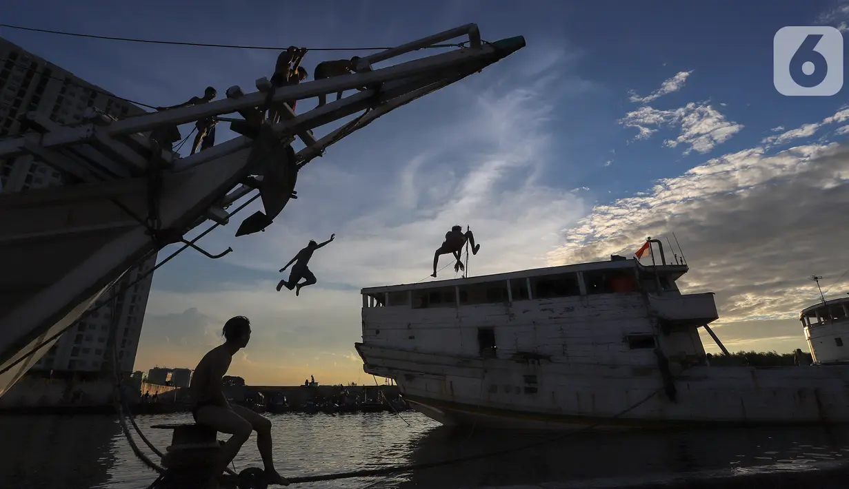 Anak-anak melompat dari atas kapal yang tengah bersandar di Pelabuhan Sunda Kelapa, Jakarta, Senin (6/7/2020). Lompatan dari atas kapal tanpa pengaman ini dilakukan sore hari menjelang matahari terbenam. (Liputan6.com/Fery Pradolo)