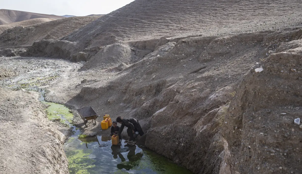 Dua bersaudara mengisi dirigen dengan air dari kolam tergenang sekitar 3 km dari rumah mereka di desa Kamar Kalagh di luar Herat, pada 26 November 2021. Kekeringan Afghanistan, yang terburuk dalam beberapa dekade, kini memasuki tahun kedua, diperburuk oleh perubahan iklim. (AP/Petros Giannakouris)