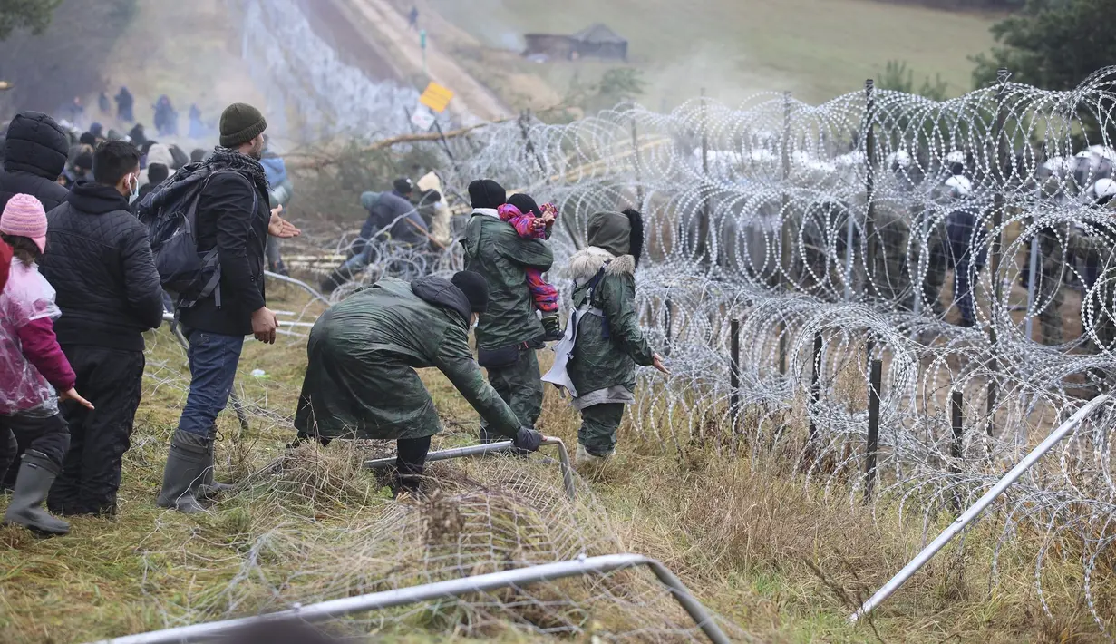 Migran dari Timur Tengah dan tempat lain mendobrak pagar saat mereka berkumpul di perbatasan Belarusia-Polandia dekat Grodno, Belarus, Senin (8/11/2021). (Leonid Shcheglov/BelTA via AP)