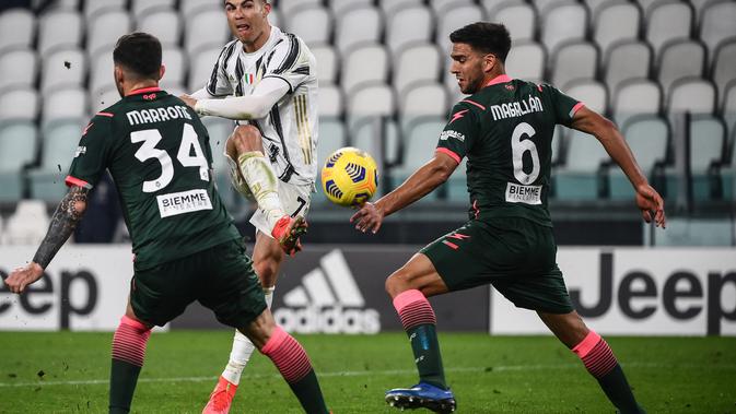 Bintang Juventus, Cristiano Ronaldo melakukan tendangan di antara pemain Crotone Luca Marrone dan Lisandro Magallan dalam lanjutan Liga Italia di Allianz Stadium, Selasa dinihari WIB (23/2/2021). Ronaldo menyumbang dua gol pada laga ini, satu gol lagi disumbang Weston McKennie (Marco BERTORELLO/AFP)