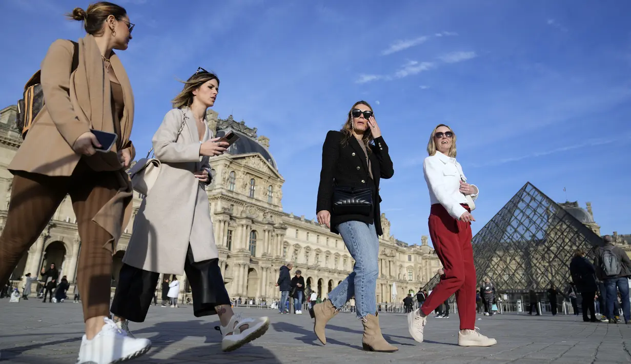 Turis tanpa mengenakan masker berjalan di sebelah Museum Louvre, di Paris, Senin (14/3/2022). Prancis telah mencabut sebagian besar pembatasan COVID-19 pada hari Senin, memungkinkan orang melepas masker di hampir semua tempat. (AP Photo/Francois Mori)