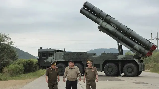 Dalam foto tidak bertanggal ini yang dipublikasikan pada hari Jumat (13/9/2024) oleh pemerintah Korea Utara, Kim Jong Un berjalan dengan pejabat lainnya di dekat apa yang disebut sebagai wahana peluncur baru roket ganda 600 mm di lokasi yang dirahasiakan.