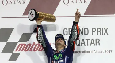 Pembalap Movistar Yamaha MotoGP, Maverick Vinales, mengangkat pialanya di atas podium setelah memenangi MotoGP Qatar di Sirkuit Losail, Doha, Minggu (26/3). Vinales menyelesaikan balapan dengan catatan waktu 38 menit 59,999 detik. (Karim JAAFAR/AFP)