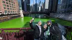 Sekelompok orang berselfie dengan latar belakang Sungai Chicago yang berwarna hijau di LaSalle Street Bridge, Sabtu (12/3/2022). Perubahan warna ini dilakukan untuk menyambut Hari St. Patrick pada Kamis mendatang. (Tyler Pasciak LaRiviere/Chicago Sun-Times via AP)