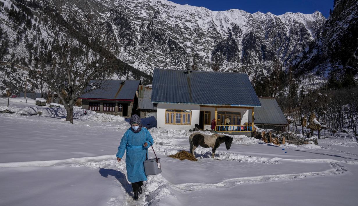 Masrat Farid, seorang petugas kesehatan, membawa vaksin saat berjalan di lapangan tertutup salju setelah memberikan dosis kepada gadis-gadis muda selama upaya vaksinasi COVID-19 di Gagangeer, timur laut Srinagar, Kashmir yang dikuasai India, pada 12 Januari 2022. (AP Photo /Dar Yasin)