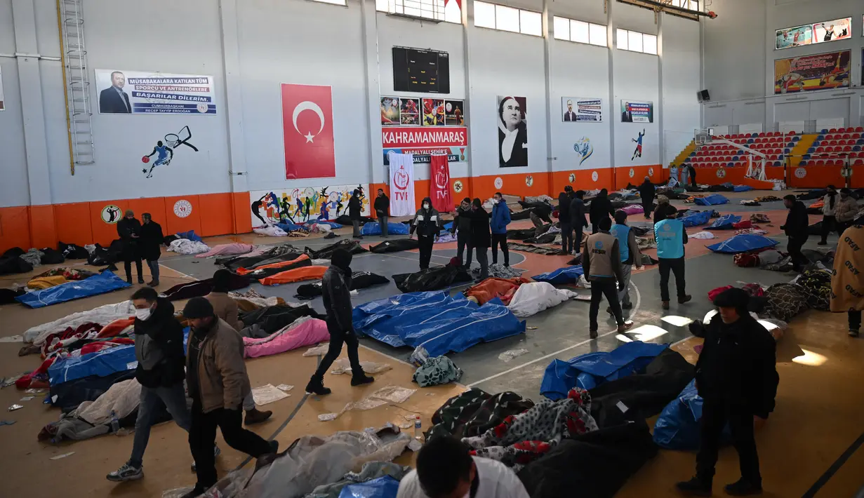 Orang-orang berjalan melewati jenazah para korban yang disimpan di gedung olahraga kota, dua hari setelah gempa kuat melanda wilayah tersebut, di kota Kahramanmaras, Turki tenggara, Rabu (8/2/2023). Korban tewas akibat gempa magnitudo (M) 7,8 yang melanda Turki dan Suriah bertambah. Tercatat sudah lebih dari 15 ribu orang meninggal akibat gempa tersebut. (OZAN KOSE / AFP)