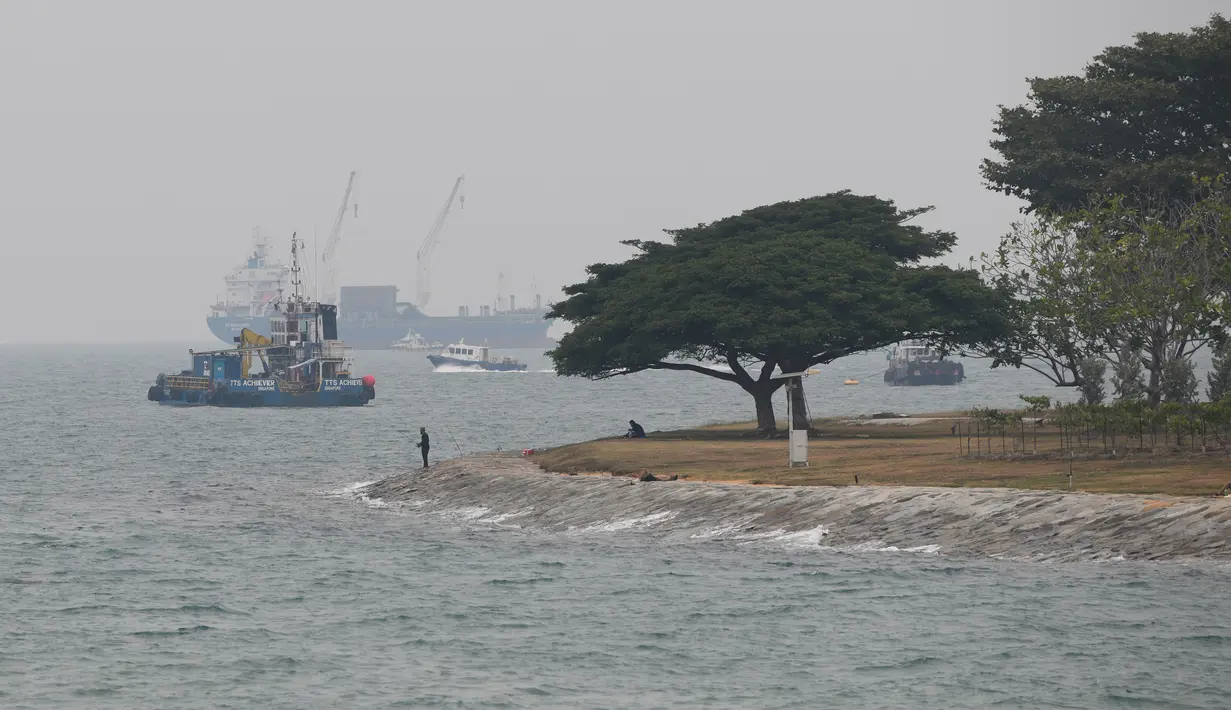 Seorang pria memancing at kabut asap menyelimuti kota Singapura (15/9/2019). Polusi dari kebakaran hutan di Indonesia mendorong kualitas udara Singapura ke tingkat yang tidak sehat untuk pertama kalinya dalam tiga tahun. (AFP Photo/Roslan Rahman)