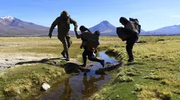 Seorang tentara Chili membantu seorang migran menyeberangi kanal air sebelum membawa mereka ke tempat penampungan di mana polisi mendaftarkan mereka, dekat Colchane, Chili, Rabu, 1 Maret 2023. Langkah tersebut adalah yang terbaru oleh pemerintah paling kiri Chile dalam 50 tahun untuk mencoba mengembalikan kemerosotan popularitasnya setelah satu tahun menjabat. (AP Photo/Ignacio Munoz)