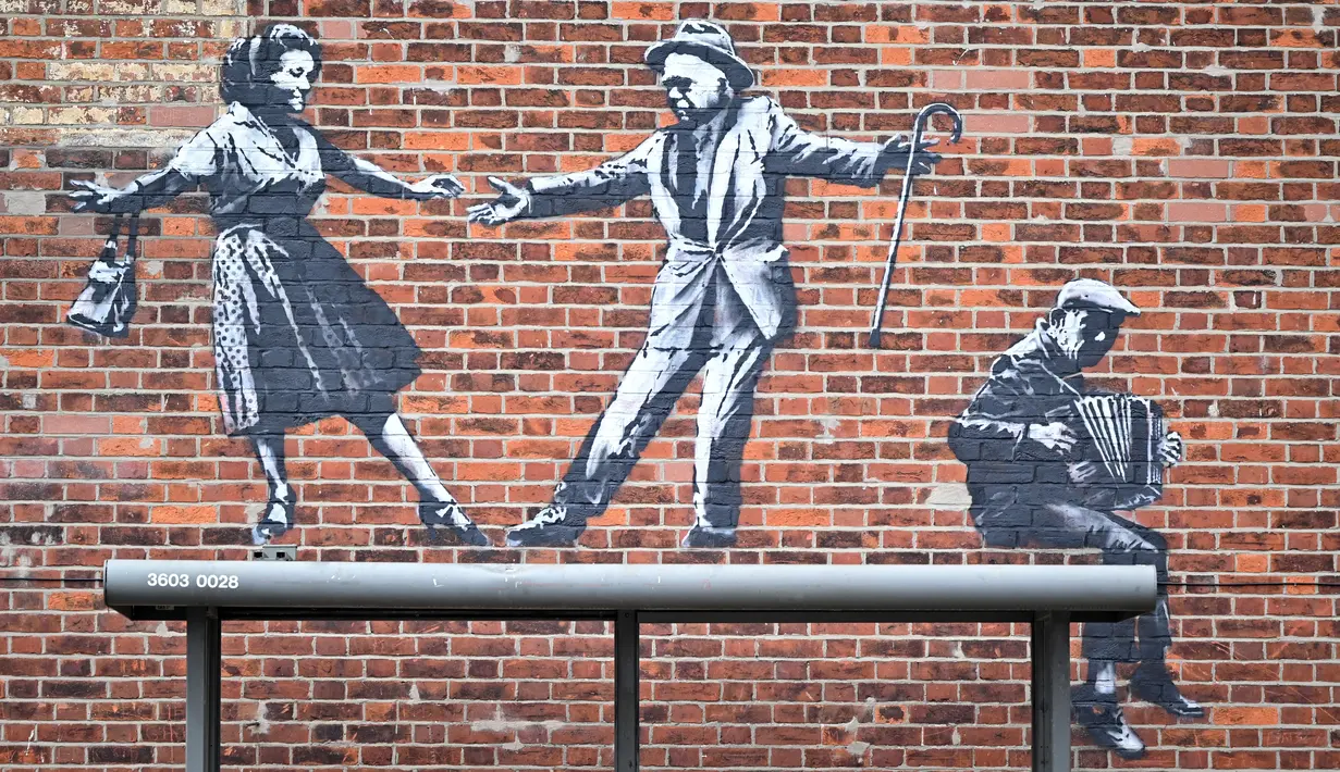 Sebuah karya seni grafiti dari pasangan yang menari dengan pemain akordeon, yang menyandang ciri khas seniman jalanan Banksy, terlihat di dinding di Great Yarmouth di pantai timur Inggris pada 8 Agustus 2021. Karya tersebut belum diklaim oleh Banksy. (JUSTIN TALLIS / AFP)