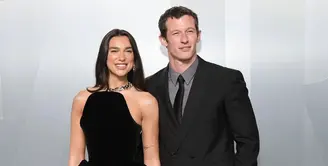 Dua Lipa tampil memukau dalam balutan gaun Schiaparelli bernuansa emas metalik dengan detail fur dramatis, menciptakan siluet sensual sekaligus bold. Ia tampak serasi dengan sang tunangan, Callum Turner, yang memilih setelan klasik bernuansa krem dengan bow tie hitam. Perpaduan mereka memancarkan aura old Hollywood glamour yang modern.