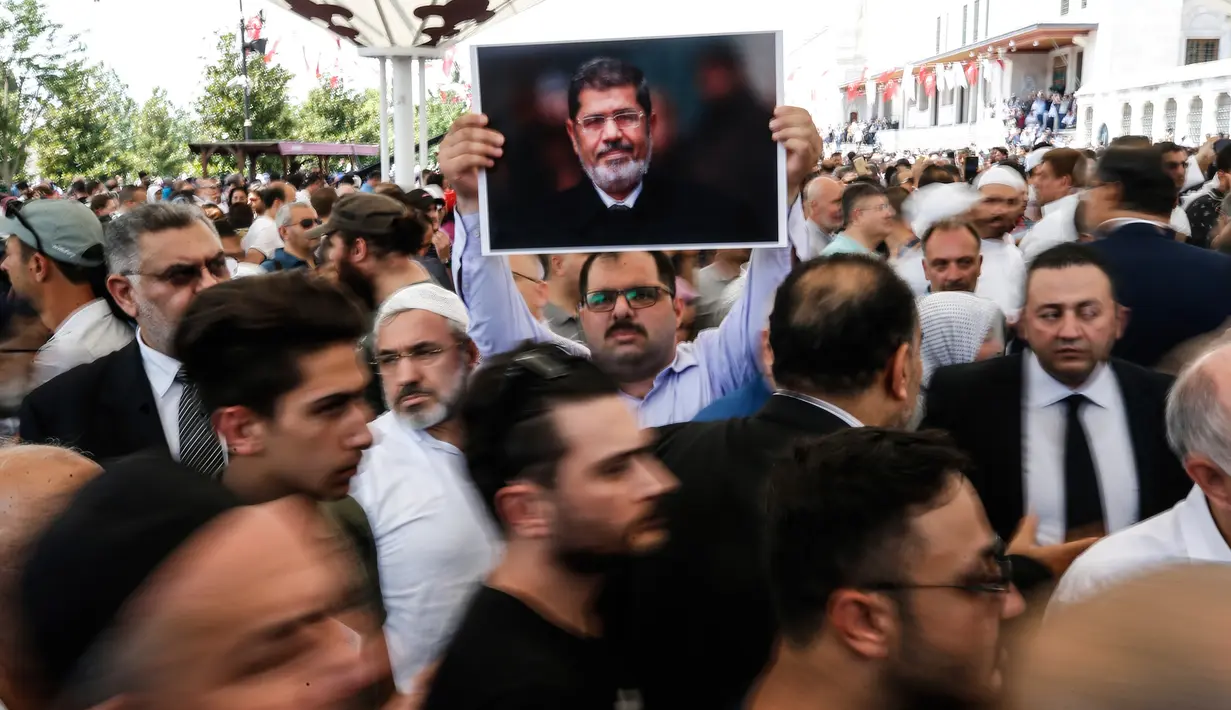 Seorang pria memegang foto mantan Presiden Mesir Mohammed Morsi sebelum menunaikan salat gaib di Masjid Fatih, Istanbul, Selasa (18/6/2019). Mohammed Morsi meninggal saat menjalani sidang atas tuduhan spionase pada Senin, 17 Juni 2019. (AP Photo/Emrah Gurel)