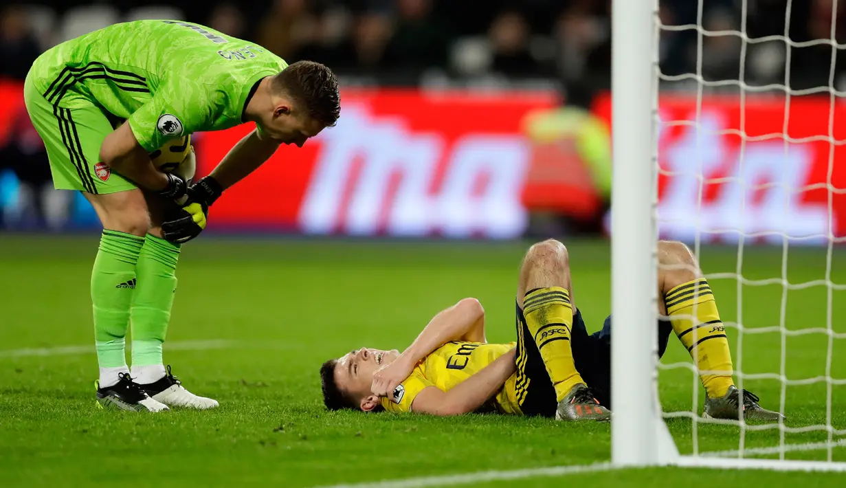Pemain Arsenal Kieran Tierney (kanan) terbaring di lapangan dan berbicara dengan kiper Bernd Leno setelah dia dilanggar pada pertandingan Liga Inggris menghadapi West Ham United di London Stadium, London, Inggris, Senin (9/12/2019). Arsenal menang 3-1. (AP Photo/Kirsty Wigglesworth)
