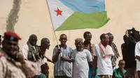 Orang-orang mengibarkan bendera nasional Djibouti sambil menunggu kedatangan Presiden Djibouti Ismail Omar Guellehas sebelum upacara peluncuran proyek pembangunan rumah baru 1000 unit di Djibouti, pada 4 Juli 2018. (YASUYOSHI CHIBA / AFP)