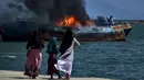 Para warga menyaksikan asap hitam mengepul dari kapal asing ilegal yang dibakar dan ditenggelamkan Kejaksaan Negeri Banda Aceh di perairan Pelabuhan Perikanan Samudera Kutaraja, Banda Aceh, Aceh, Kamis (18/3/2021). (AFP/Chaideer Mahyuddin)