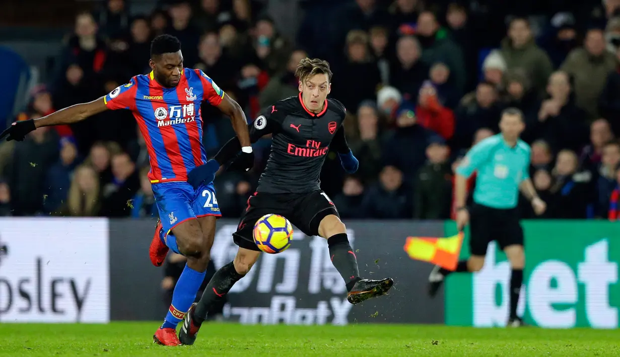 Pemain Arsenal, Mesut Ozil berebut bola dengan pemain Crystal Palace Timothy Fosu-Mensah saat pertandingan Liga Inggris di stadion Selhurst Park di London (28/12). Arsenal menang tipis 2-3 atas tuan rumah Crystal Palace. (AP Photo/Alastair Grant)