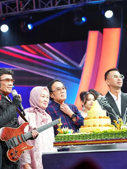Acara tersebut berlangsung dengan nuansa penuh budaya dan kebahagiaan. Tumpeng kuning berukuran besar menjadi pusat perhatian di atas panggung, dikelilingi oleh makanan tradisional yang melambangkan syukur dan kehangatan. Kehadiran Rhoma Irama dengan kostum hitam beraksen merah, serta gitarnya yang ikonik, menambah kesan istimewa pada momen tersebut. (Liputan6.com/IG/@raffinagita171