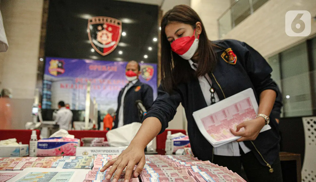 Petugas merapikan uang palsu saat rilis di Gedung Lobby Bareskrime Mabes Polri, Jakarta, Kamis (23/9/2021). Pemalsuan dan peredaran uang palsu dilakukan sejak Agustus-September 2021 sebanyak 20 orang diamankan dan ditetapkan sebagai tersangka. (Liputan6.com/Faizal Fanani)