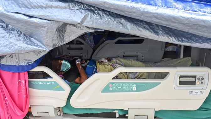 Seorang pria yang terluka dalam gempa dengan magnitudo 6,2 beristirahat di tempat penampungan sementara di luar Rumah Sakit Regional Sulbar, Mamuju, Sulawesi Barat, Minggu (17/1/2021). Mereka dirawat di dalam tenda darurat untuk mengantisipasi gempa susulan. (ADEK BERRY/AFP)