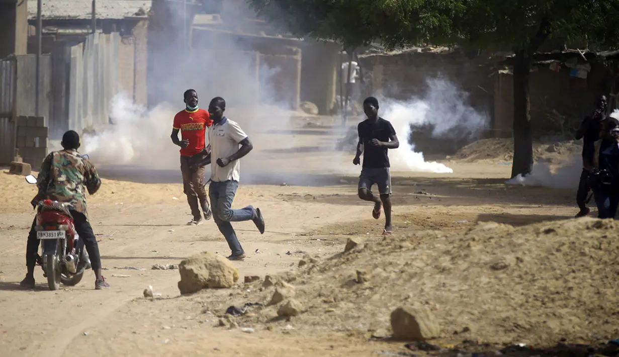 Para pengunjuk rasa menyelamatkan diri setelah terkena gas air mata oleh polisi di N'Djamena, Chad, Selasa (27/4/2021). Ribuan orang melakukan protes dan dua orang tewas dalam demonstrasi menentang aturan dewan militer transisi yang dipimpin putra Presiden Idriss Deby. (AP Photo/Sunday Alamba)