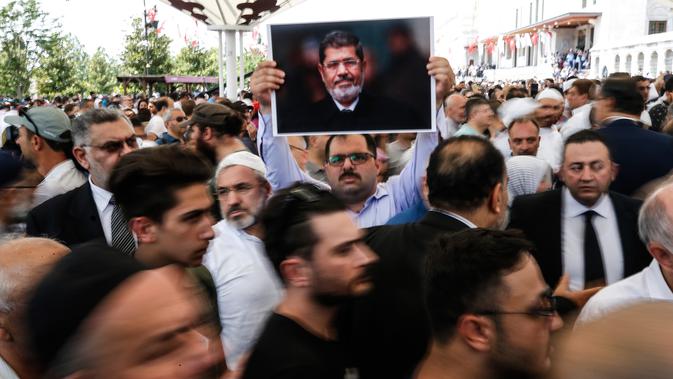 Seorang pria memegang foto mantan Presiden Mesir Mohammed Morsi sebelum menunaikan salat gaib di Masjid Fatih, Istanbul, Selasa (18/6/2019). Mohammed Morsi meninggal saat menjalani sidang atas tuduhan spionase pada Senin, 17 Juni 2019. (AP Photo/Emrah Gurel)