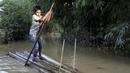 Seorang anak laki-laki berjalan dengan rakit bambu melalui air banjir di daerah Kanaighat di Sylhet, Bangladesh (23/5/2022). Banjir bandang pra-musim telah membanjiri bagian dari India dan Bangladesh, menewaskan sedikitnya 24 orang dalam beberapa pekan terakhir dan mengirim 90.000 orang ke tempat penampungan. (AP Photo)