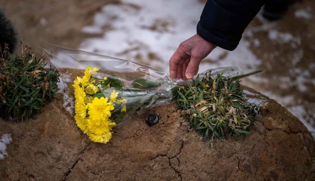 Seorang pria meletakkan bunga di makam seorang kerabatnya dalam upacara peringatan satu tahun dimulainya perang Rusia-Ukraina, di sebuah pemakaman di Bucha, Ukraina, Jumat, 24 Februari 2023. (AP Photo/Emilio Morenatti)
