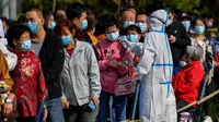 Petugas medis mengukur suhu warga saat mereka antre untuk tes COVID-19 di dekat daerah perumahan di Qingdao, China, Senin (12/10/2020). Lebih dari 9 juta orang yang tinggal di kota Qingdao, menjalani tes virus Corona (COVID-19) secara massal setelah muncul kasus baru. (STR/AFP)