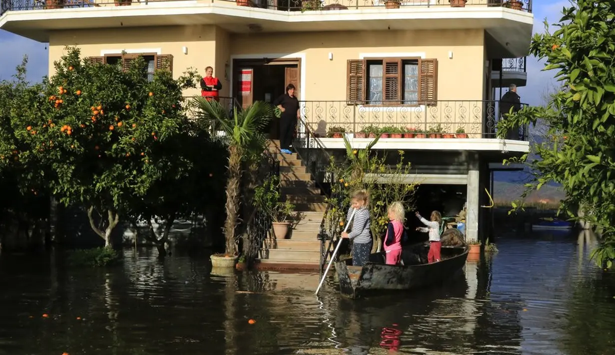 Anak-anak menaiki sampan di luar rumah yang banjir usai hujan lebat di Desa Obot, sekitar 100 kilometer (60 mil) barat laut Tirana, Albania, Senin (11/1/2021). Pihak berwenang mengevakuasi banyak warga menyusul banjir yang merendam ribuan hektare (acre) kawasan di Albania. (AP Photo/Hektor Pustina)