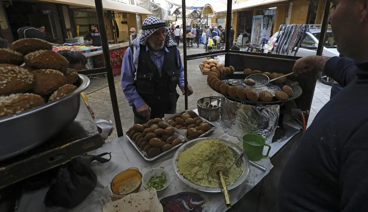 Seorang pria Palestina menunggu sejumlah falafel di sebuah penjual di kota Hebron di Tepi Barat yang diduduki, selama bulan suci Ramadhan, Minggu (18/4/2021). Falafel adalah sebuah makanan Timur Tengah yang pada bulan Ramadhan, sering dimakan sebagai hidangan buka puasa. (HAZEM BADER/AFP)