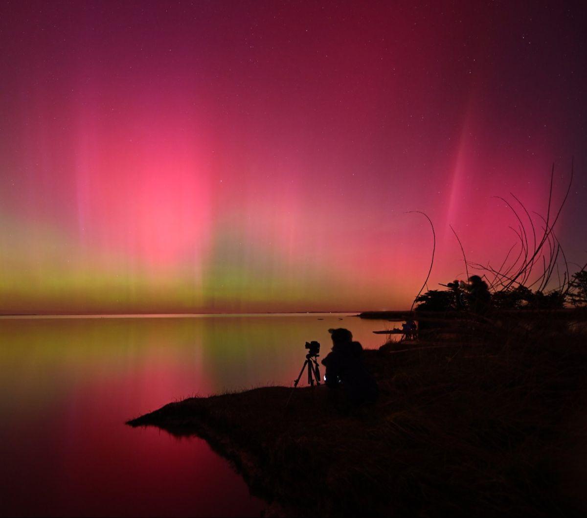 Seorang fotografer mengabadikan Aurora Australis yang menghiasi langit&nbsp;di atas perairan Danau Ellesmere, Christchurch, Selandia Baru, Sabtu (11/5/2024). Terlihat begitu indah dengan warna-warni cahaya yang menari-nari, namun ternyata aurora langka in