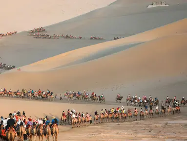 Para wisatawan menaiki unta di padang pasir di Dunhuang di provinsi Gansu di China barat laut (10/8/2019). Dunhuang adalah sebuah kota tingkat kabupaten di barat laut provinsi Gansu, Tiongkok Barat. (AFP Photo/Str)