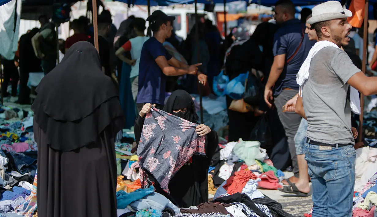 Seorang wanita Palestina berbelanja pakaian di sebuah pasar tradisional yang kembali dibuka setelah pelonggaran karantina wilayah COVID-19  di kamp pengungsi Nuseirat di Jalur Gaza tengah, Senin (13/7/2020). (AFP/Mohammed Abed)