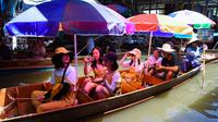 Wisatawan naik perahu di pasar terapung Damnoen Saduak, Bangkok, Thailand, Jumat (21/6/2019). Paling enak, datang ke sini untuk berwisata kuliner karena itulah yang menjadi salah satu daya tarik Thailand yakni street food. (TANG CHHIN Sothy/AFP)