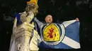 Seorang pendukung Skotlandia mengibarkan bendera di patung William Shakespeare di Leicester Square, London, Jumat (18/6/2021). (AP/Kirsty Wigglesworth)