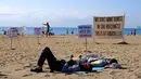 Dua pria berbaring di atas pasir saat sejumlah orang melakukan aksi protes di pantai Barcelona, Sabtu (12/8). Sejumlah aktivis menunjukkan ketidakpuasan dengan meningkatnya kedatangan wisatawan ke Spanyol. (AP Photo/Manu Fernandez)