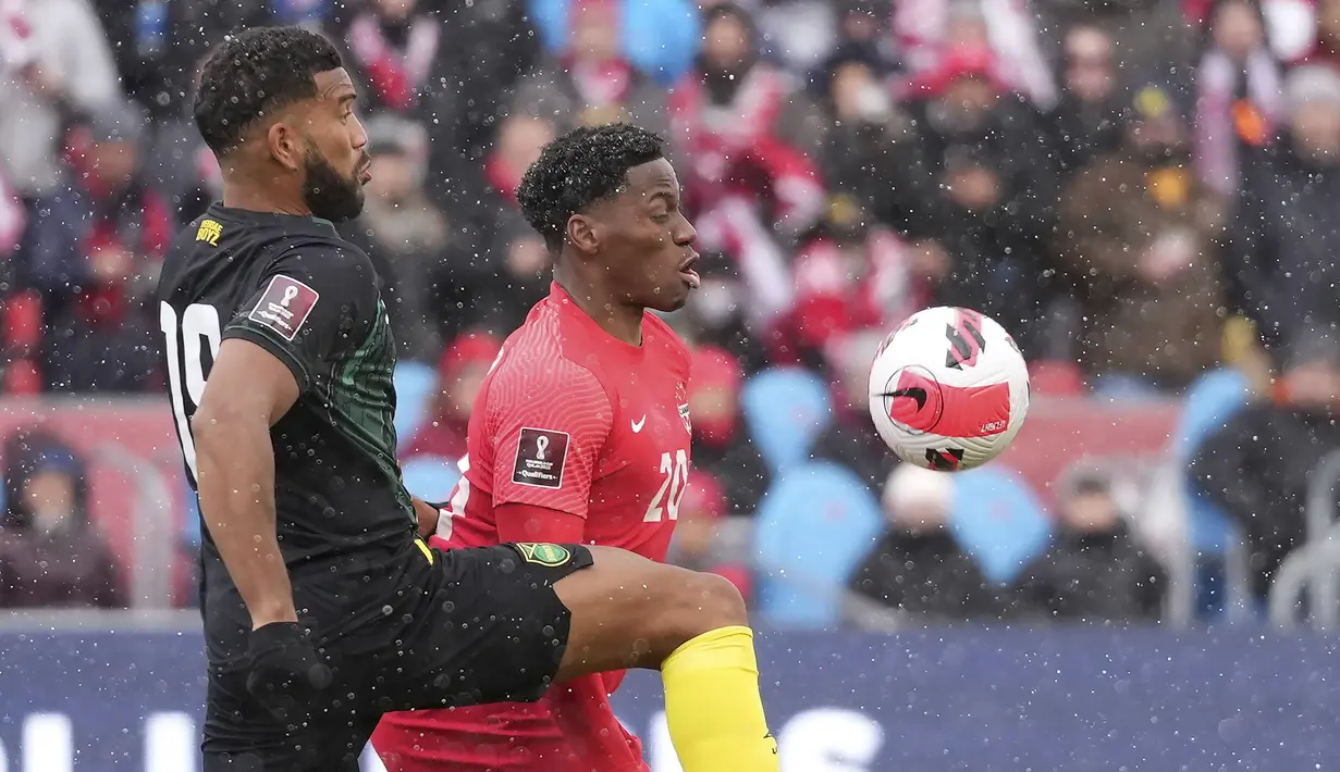 Penyerang timnas Kanada Jonathan David dan bek Jamaika Adrian Mariappa berebut bola pada Kualifikasi Piala Dunia 2022 Zona CONCACAF di Venue BMO Field, Senin (28/3/2022) dini hari WIB. Kanada lolos ke Piala Dunia 2022 usai melibas Jamaika dengan skor 4-0. (Nathan Denette/The Canadian Press via AP)