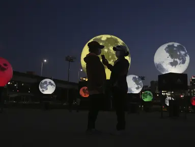 Wanita berdiri di samping instalasi bulan purnama yang bersinar di sebuah taman di Seoul, Korea Selatan, Jumat (18/9/2020). Pejabat setempat memasang bulan purnama buatan untuk meningkatkan semangat saat wabah COVID-19 sekaligus menyambut Chuseok, Thanksgiving versi Korea. (AP Photo/Ahn Young-joon)