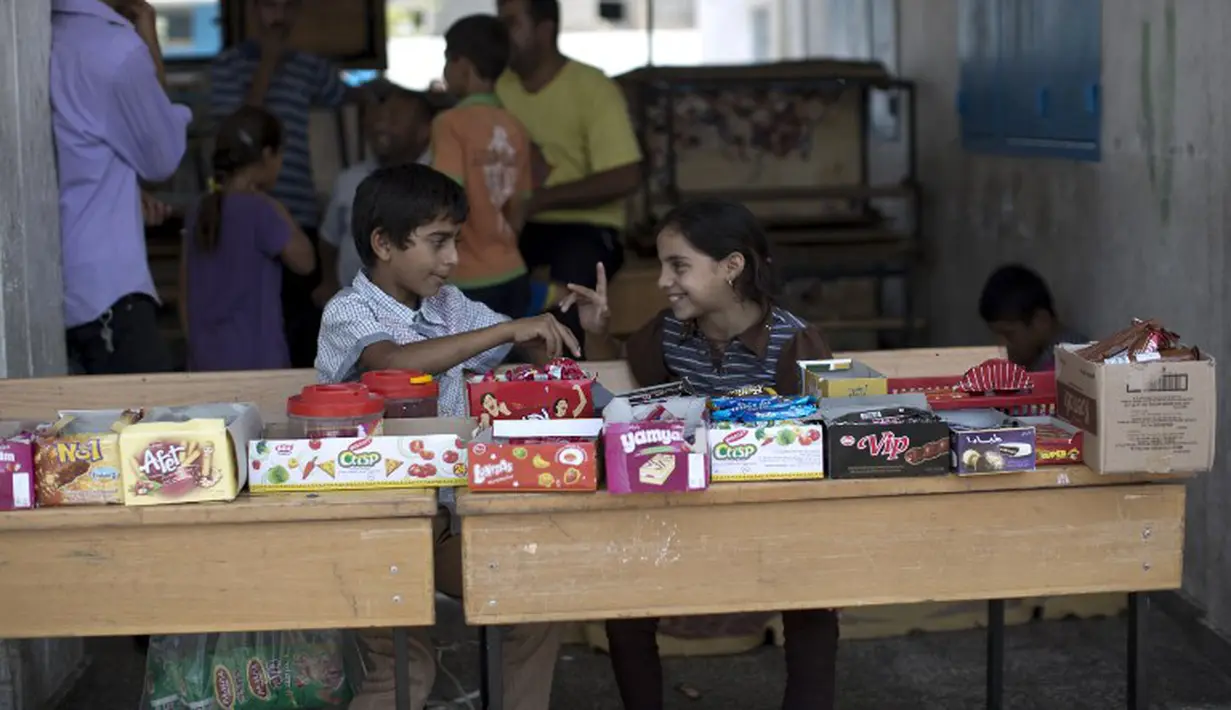 Anak-anak Palestina duduk di depan warung yang berada di kamp pengungsi Sekolah PBB di Jabalia, Gaza (28/7/14). (AFP PHOTO/MOHAMMED ABED)