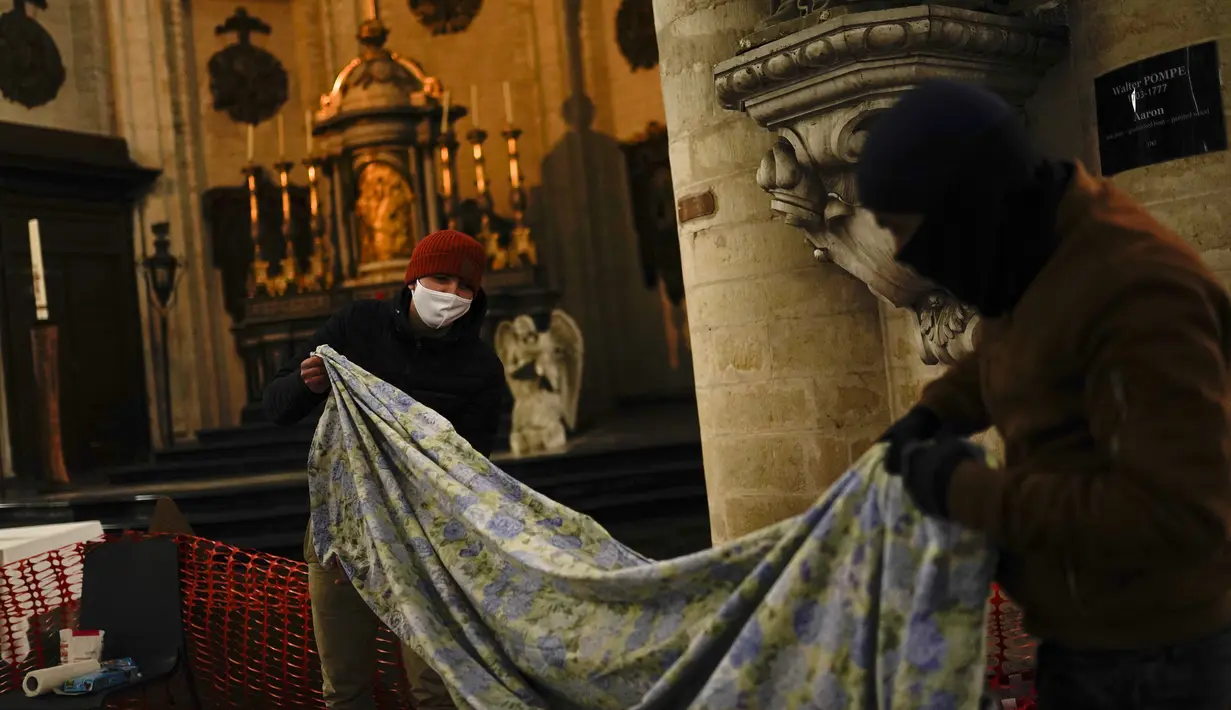 Dua pria melipat seprai dan selimut saat mereka menempati gereja Saint-Jean-Baptiste-au-Beguinage di Brussels, Belgia, Selasa (2/2/2021). Beberapa ratus imigran tanpa surat resmi, dengan izin pastor, telah menduduki gereja sejak Minggu, 31 Januari 2021 lalu. (AP Photo/Francisco Seco)