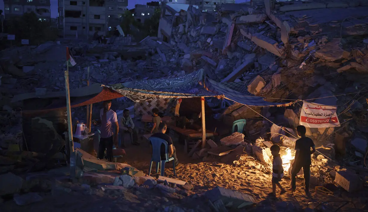 Warga Palestina duduk dalam tenda darurat yang dibangun di antara puing-puing rumah mereka yang hancur karena serangan udara Israel di Beit Lahia, Jalur Gaza, Jumat (4/6/2021). Gencatan senjata yang mengakhiri perang 11 hari antara Hamas dan Israel telah lama dilakukan. (AP Photo/Felipe Dana)