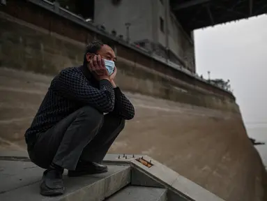 Seorang pria yang memakai masker wajah melihat ke Sungai Yangtze di Wuhan (20/11/2020). Dari total 50.340 kasus yang positif di Wuhan, 3.869 orang telah meninggal dunia akibat Covid-19 dan yang sembuh 46.471 orang. (AFP/Hector Retamal)