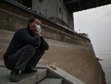 Seorang pria yang memakai masker wajah melihat ke Sungai Yangtze di Wuhan (20/11/2020). Dari total 50.340 kasus yang positif di Wuhan, 3.869 orang telah meninggal dunia akibat Covid-19 dan yang sembuh 46.471 orang. (AFP/Hector Retamal)
