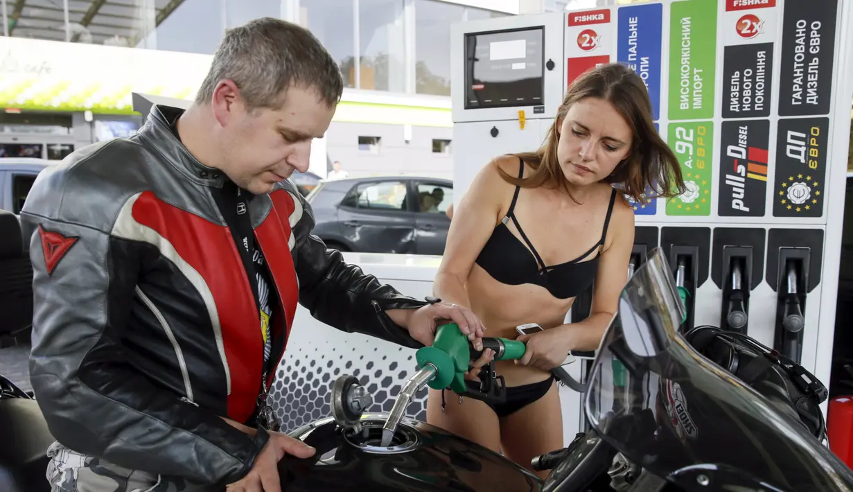 Seorang pria membantu pacarnya yang mengenakan bikini untuk mengisi bahan bakar di SPBU di Kiev, Ukraina, 26 September 2015. SPBU ini memberikan bensin gratis kepada pelanggan wanita yang datang dengan hanya mengenakan bikini. (REUTERS/Valentyn Ogirenko)