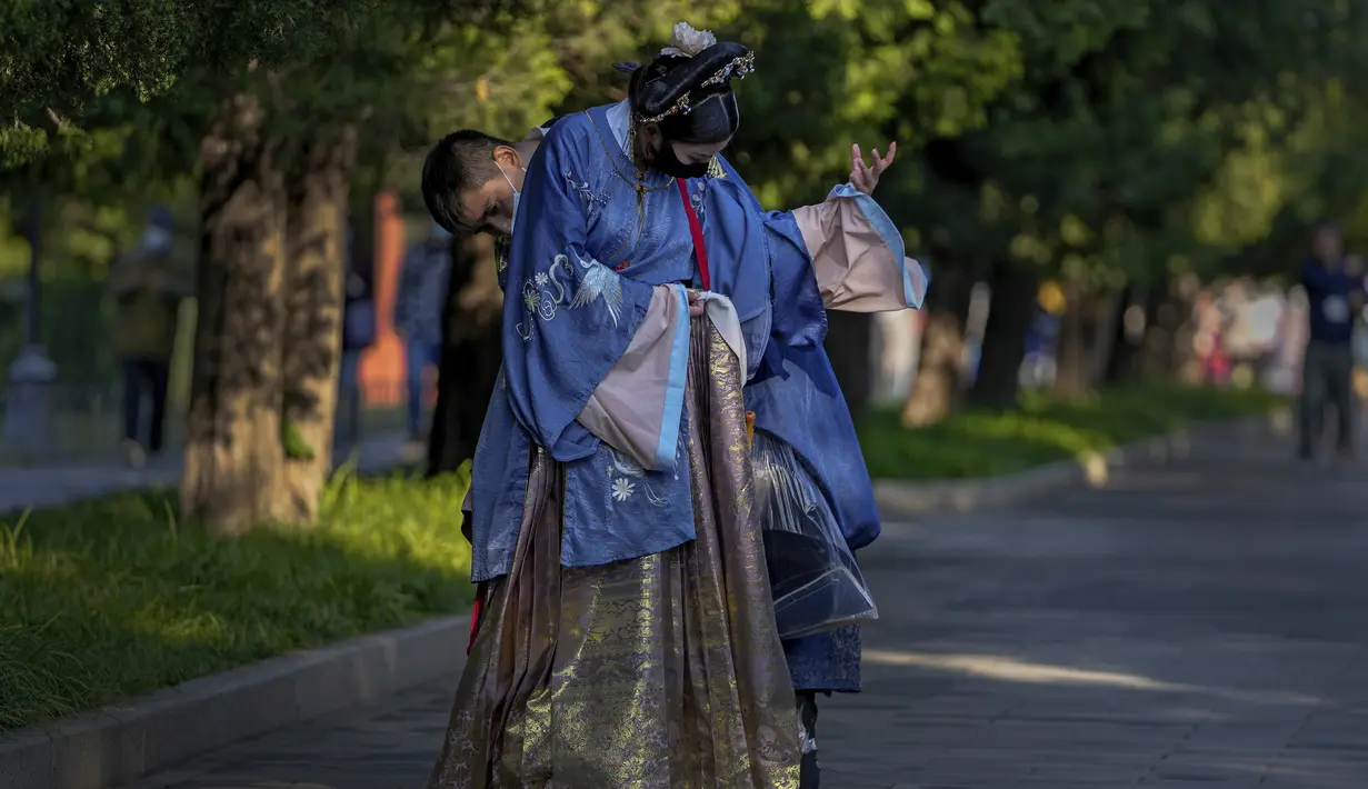Seorang pria membantu pasangannya mengenakan kostum tradisional saat mereka mengunjungi Kuil Surga pada hari terakhir Hari Nasional China selama seminggu di Beijing (7/10/2021). (AP Photo/Andy Wong)