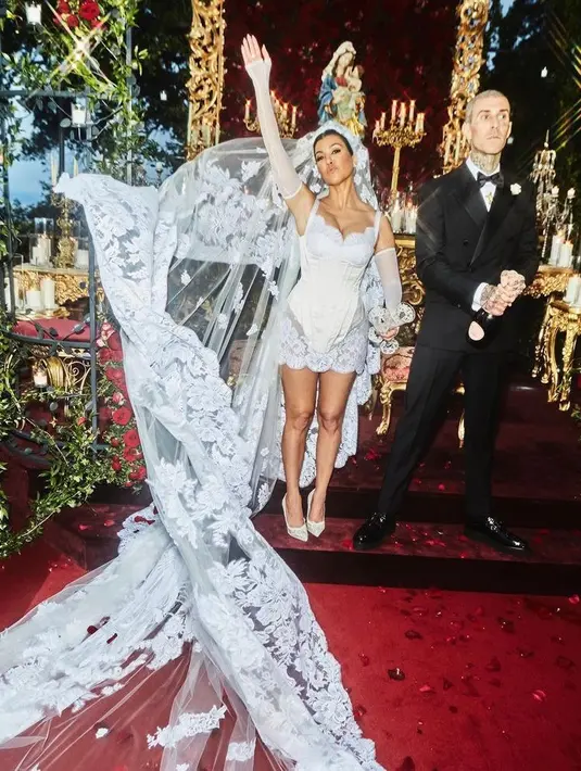 Di momen ini, Kourtney tampil memesona berbalut mini dress putih berbahan lace dengan veil panjang dramatis dari Dolce & Gabbana. Sementara Travis tampil dengan jas double breasted hitam juga dirancang oleh rumah Italia. (Instagram/kourtneykardashian).