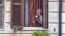 Seorang wanita bermain panci di jendala rumahnya selama flash mob di seluruh Italia untuk menyatukan orang-orang dan mencoba mengatasi darurat virus corona Covid-19 di lingkungan Garbatella, di Roma, Jumat (13/3/2020). (Cecilia Fabiano/LaPresse via AP)