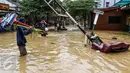 Seorang pedagang membawa dagangannya melewati banjir di kompleks Pondok Gede Permai, Jatiasih, Bekasi, Jumat (22/4). Pedagang berjualan alat kebersihan untuk membersihkan sisa lumpur yang terbawa banjir di kawasan tersebut. (Liputan6.com/Fery Pradolo)