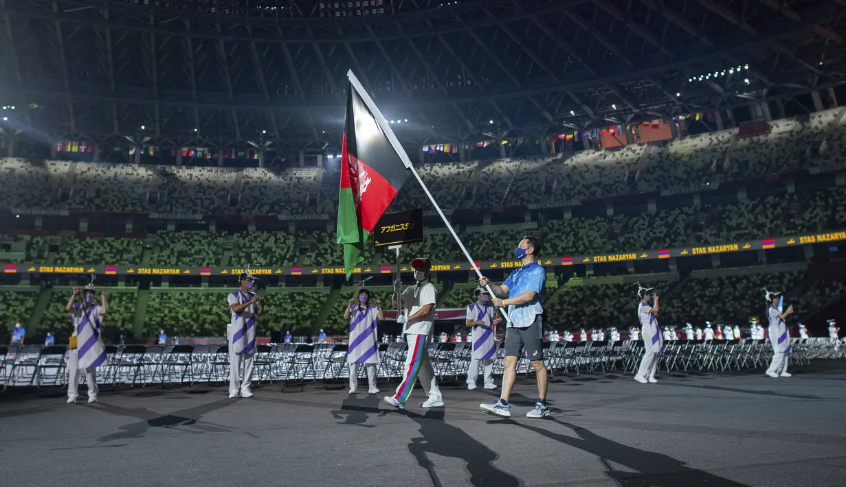 Seorang relawan membawa bendera nasional Afghanistan dalam defile upacara pembukaan Paralimpiade Tokyo 2020 di Tokyo, Selasa (24/8/2021). Bendera Afghanistan dikibarkan tanpa kehadiran satu pun atletnya menyusul kondisi negaranya pasca dikuasai oleh Taliban. (Joel Marklund for OIS via AP)